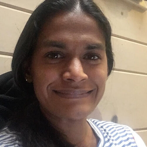 mekala-sundaram--500x500 A faculty and scientist at SREL, a woman with long dark hair smiles at the camera while seated indoors against a beige wall with horizontal lines.