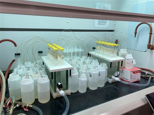 Laboratory setup with multiple plastic bottles, sample tubes, yellow-capped vials, and tubing for a chemical or biological experiment inside a fume hood, supporting UGA research on PFAS contamination in aquatic ecosystems.